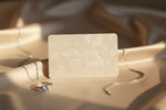 A luxurious, minimalist image of a Diamelys gift card placed elegantly on a soft ivory or champagne background. The card should feature a subtle diamond motif or embossed shimmer texture, exuding sophistication and refinement. Surround it with delicate jewelry elements — a diamond ring or necklace softly out of focus — to hint at elegance and gifting. The lighting should be warm and natural, creating a sense of intimacy and luxury. No text or logo, just a premium aesthetic that reflects Diamelys’ brand.
